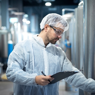 A man dressed in a white coat, hair net and safety classes is running an experiment.